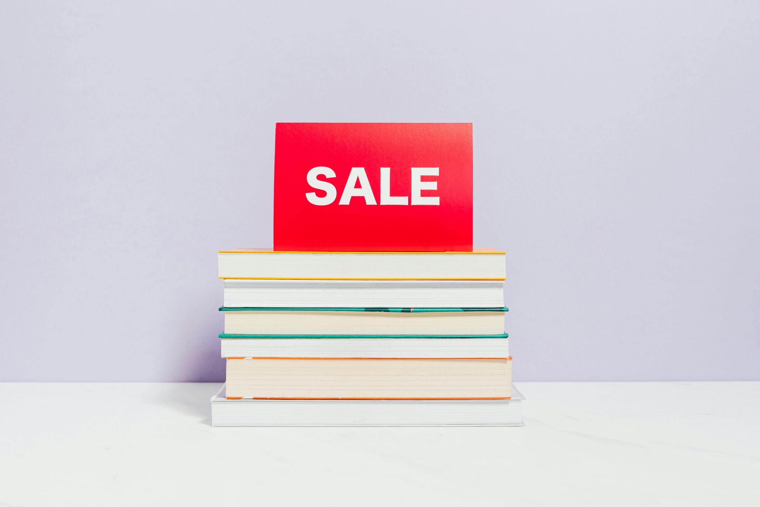 A stack of books with a red sale sign, ideal for promotions and bookshop advertisements.